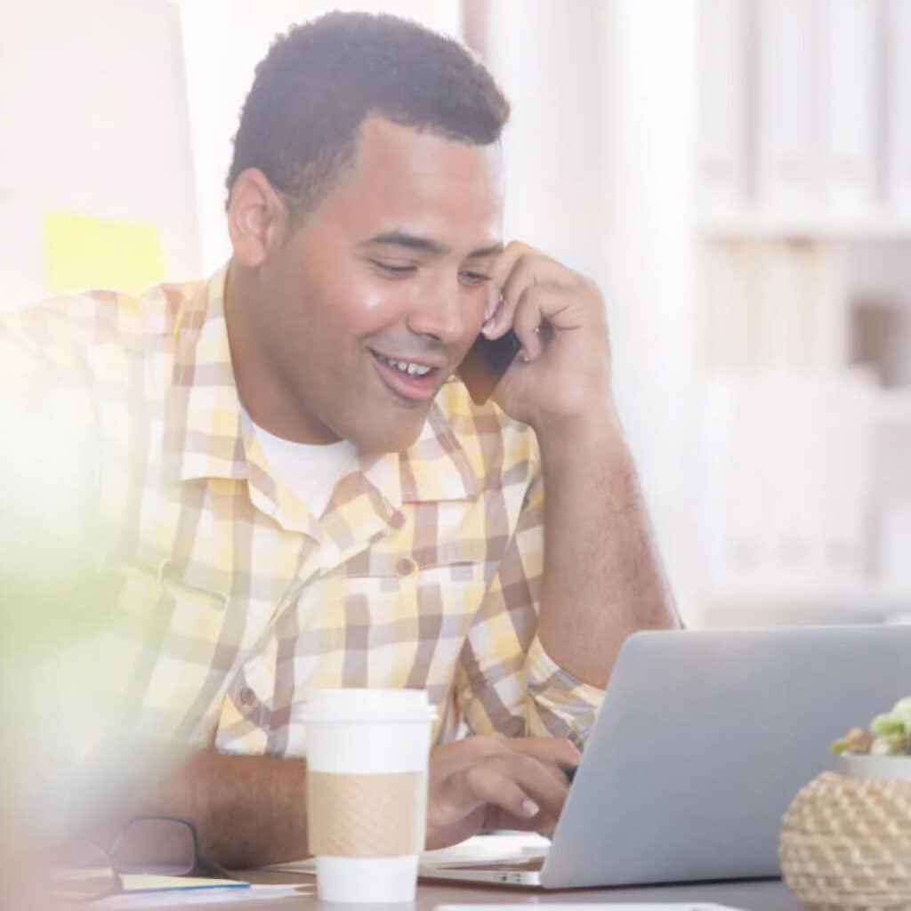 Man talking on the phone at his laptop.