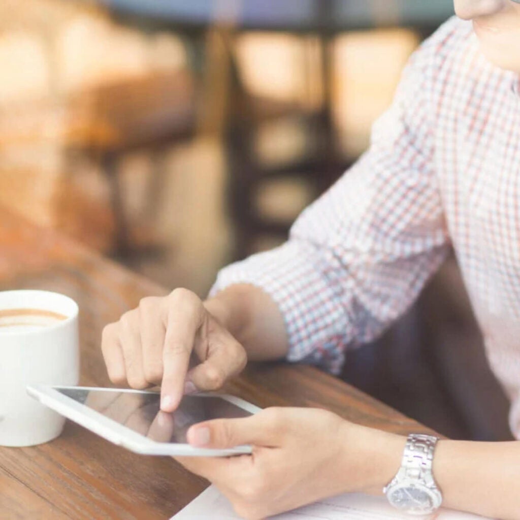 Close-up of someone using a tablet at a coffee shop.